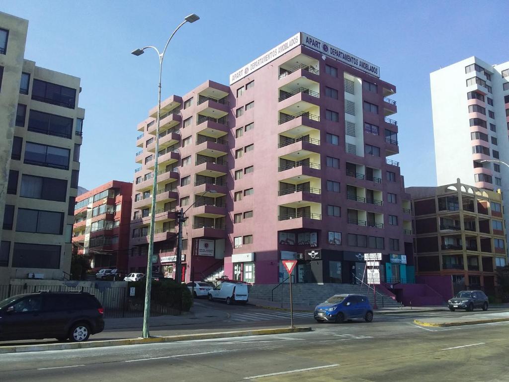 安托法加斯塔Apart Antofagasta的一座高大的粉红色建筑,汽车停在停车场