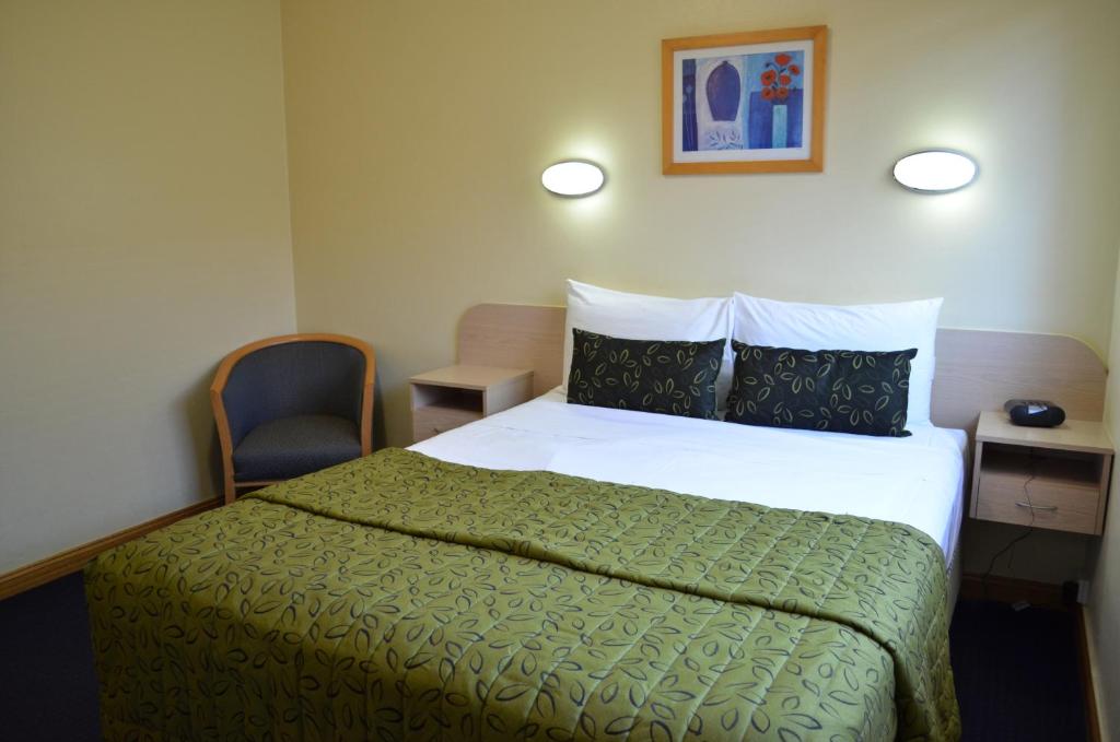 布里斯班Airport Motel Brisbane的一间卧室配有一张带绿毯的床和一把椅子