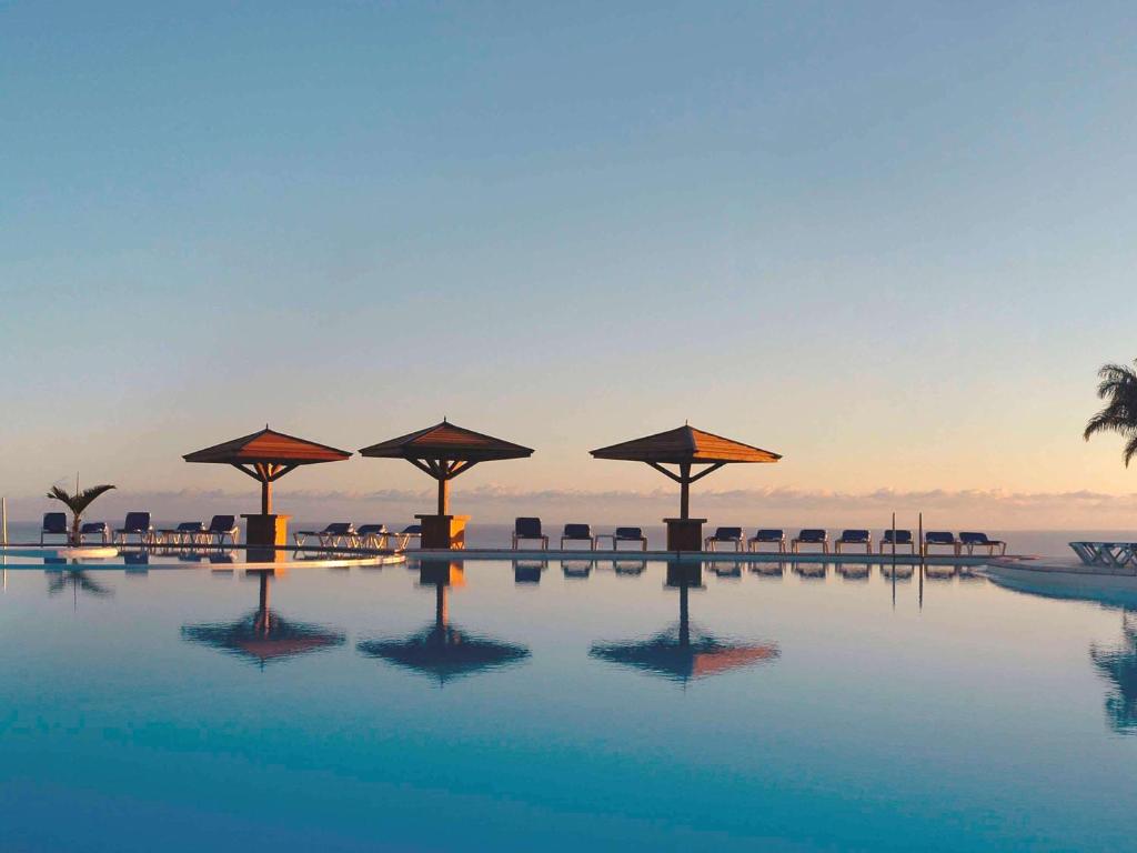 圣丹尼斯Hôtel Exsel Créolia的一座带遮阳伞的游泳池,其背景是大海