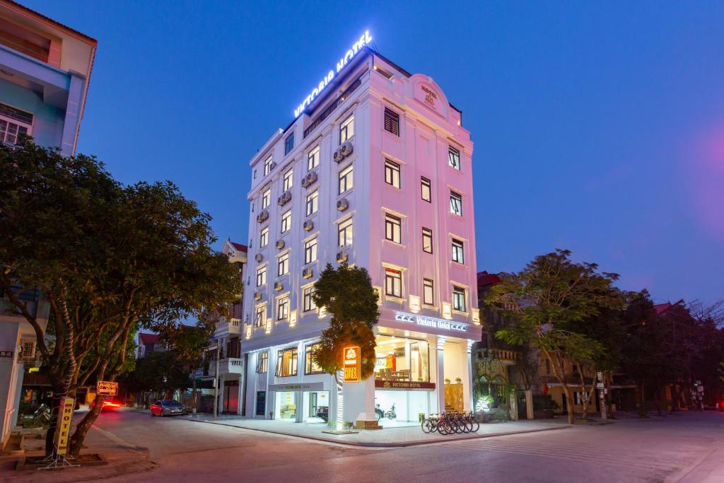 宁平Victoria Hotel Ninh Binh的夜晚在城市街道上一座高大的粉红色建筑