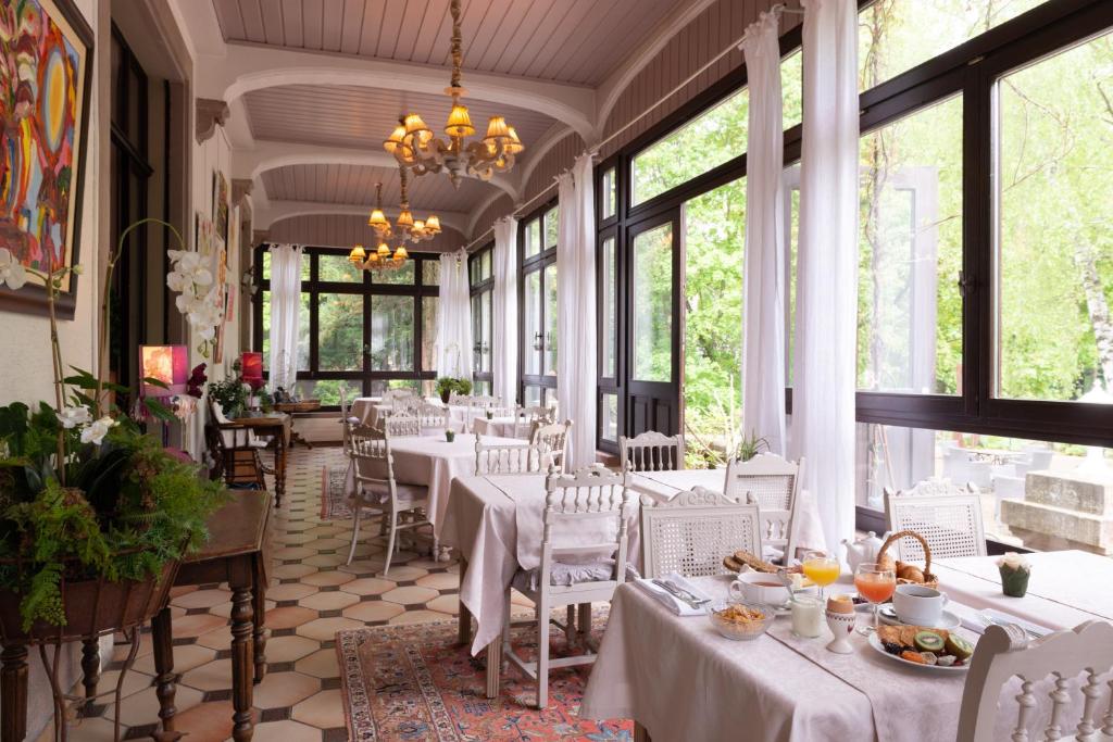 盖布维莱尔Domaine de Beaupré - Hotel The Originals Relais的餐厅设有白色的桌椅和窗户。