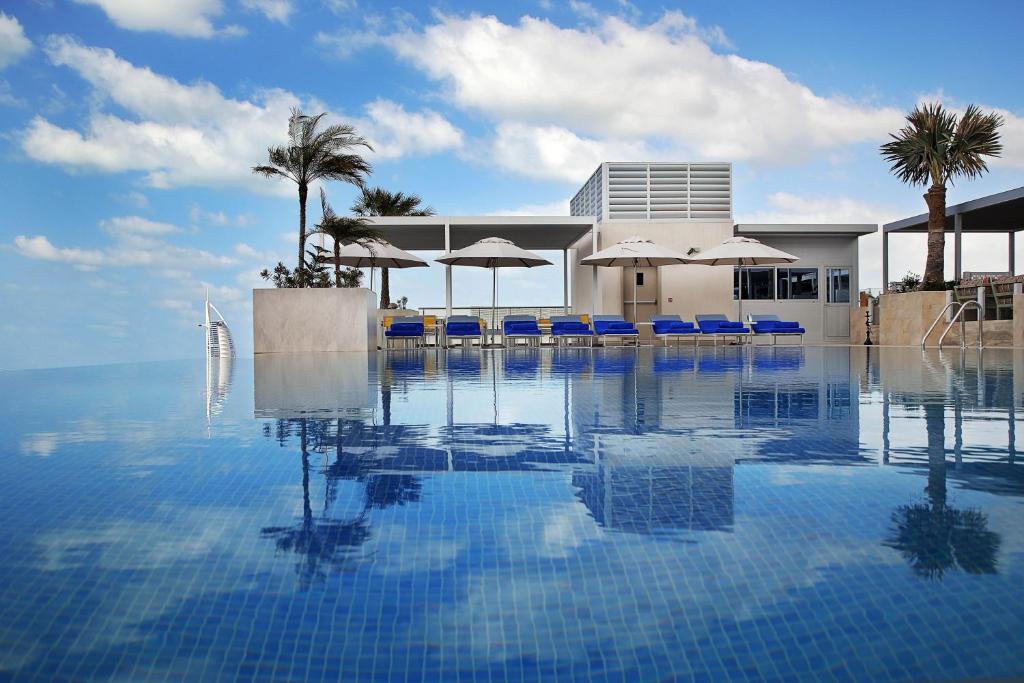 迪拜Grand Cosmopolitan Hotel的一个带蓝色椅子和遮阳伞的游泳池