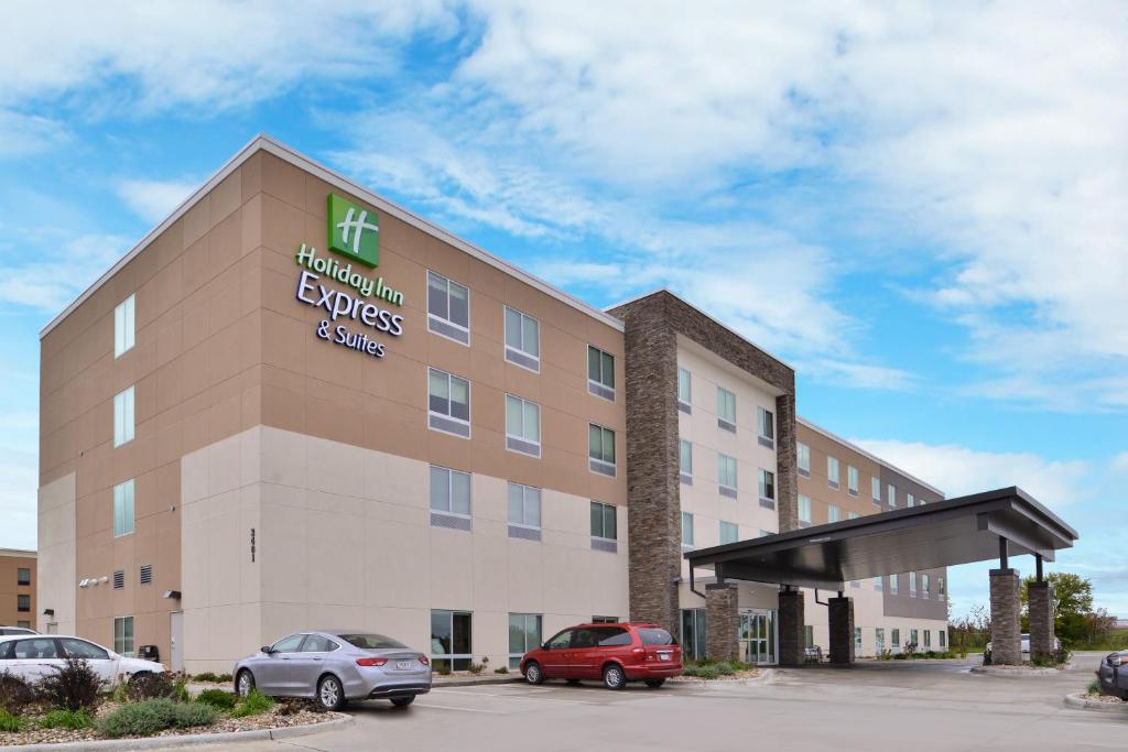 马歇尔敦Holiday Inn Express & Suites - Marshalltown, an IHG Hotel的停车场内停放汽车的酒店大楼