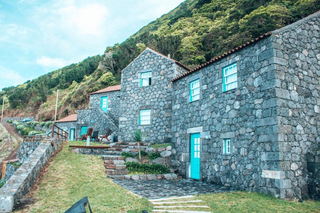 CalhetaAbrigo da Cascata - Casas de Campo - São Jorge的山前有蓝色门的石头房子