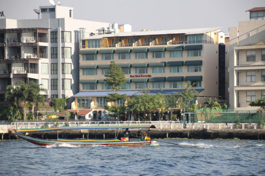 曼谷New Siam Riverside - SHA Certified的船在水中,在建筑物前