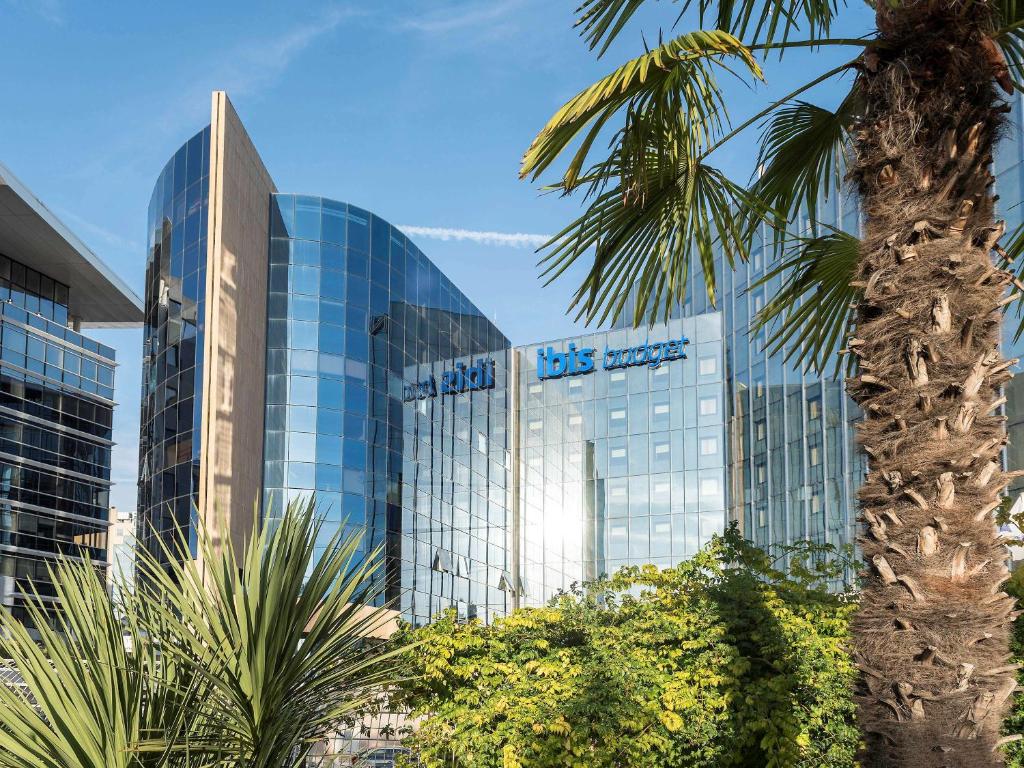 尼斯尼斯机场宜必思快捷酒店 的一座高大的玻璃建筑,前面有一棵棕榈树