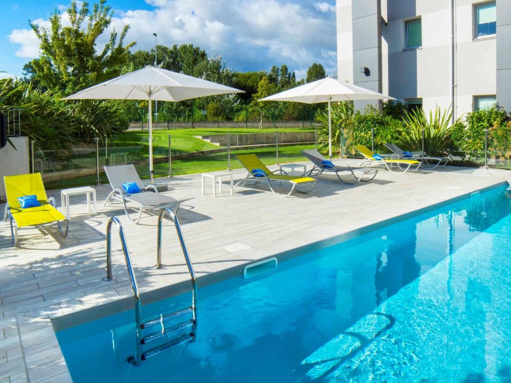 瓦朗斯瓦朗斯宜必思快捷酒店的一座带椅子和遮阳伞的游泳池位于一座建筑旁边