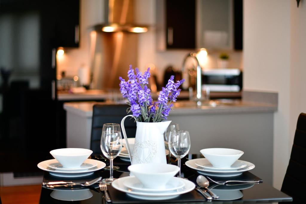 斯旺西Just Stay Wales - Meridian Quay Apartments的一张带眼镜的桌子和一个带紫色花卉的花瓶
