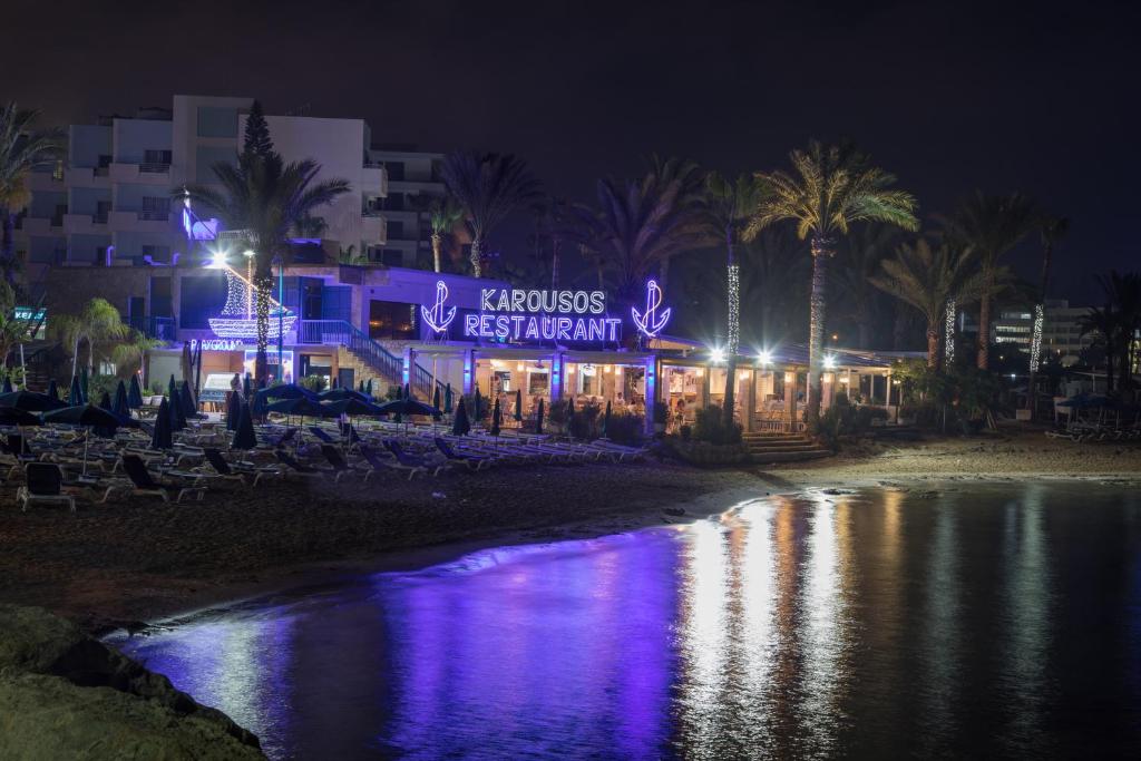 阿依纳帕Karousos Beach Rooms的海滩上的一个晚上有标志的建筑