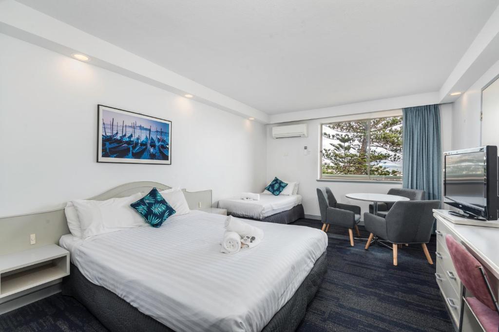 纽卡斯尔Alloggio Newcastle Beach的酒店客房带两张床和一张桌子以及椅子。