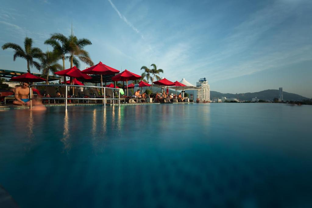 芭东海滩The Charm Resort Phuket - SHA Certified的一个带红色遮阳伞的游泳池,且有客人坐在游泳池内