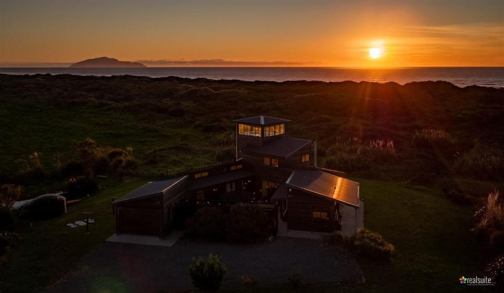 Otaki BeachIdyllic ocean front beach house - Waikawa Beach的享有房子的空中景色,背景是日落