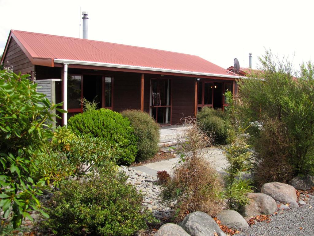 奥阿库尼Alpine Cabin - Ohakune Holiday Home的一座有红色屋顶和灌木的房子