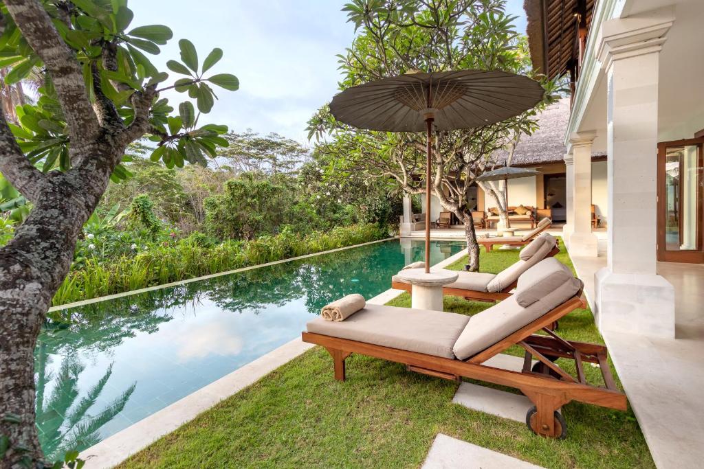 卡朗阿森Villa Perle an Idyllic Luxury Retreat的户外庭院设有2把躺椅和1把遮阳伞,毗邻游泳池