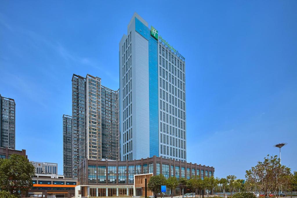 伊川Holiday Inn Express Luoyang Yichuan, an IHG Hotel的一座高大的蓝色建筑,位于一些高大的建筑前