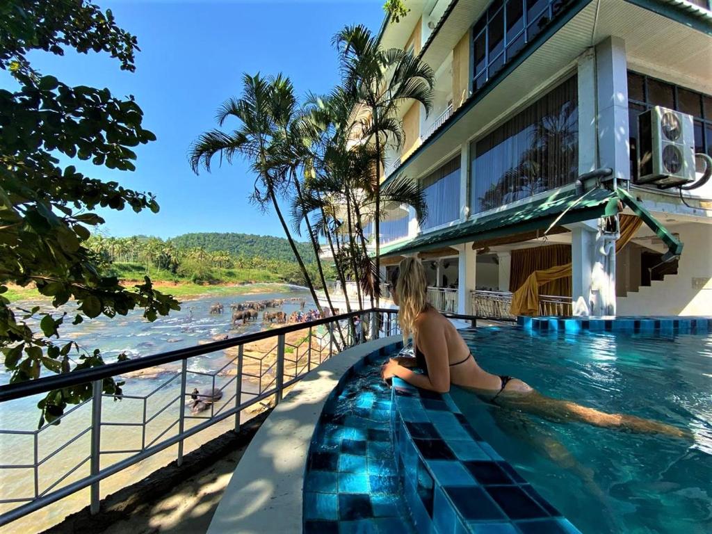 平纳瓦拉Hotel Elephant Park "Grand Royal Pinnalanda"的坐在海滩旁游泳池边的女人