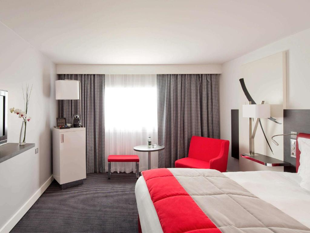 鲁瓦西昂法兰西巴黎戴高乐机场及会议中心美居酒店的酒店客房,配有一张床和一张红色椅子