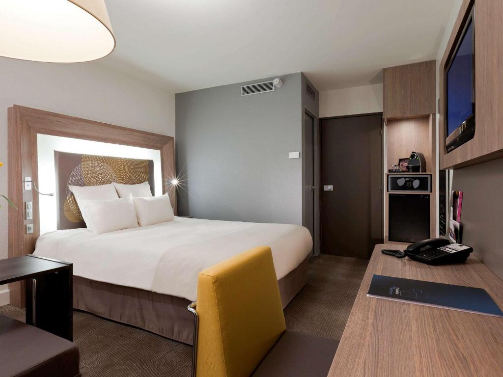 库尔布瓦Novotel Paris La Defense Esplanade的酒店客房设有一张大床和一张书桌。