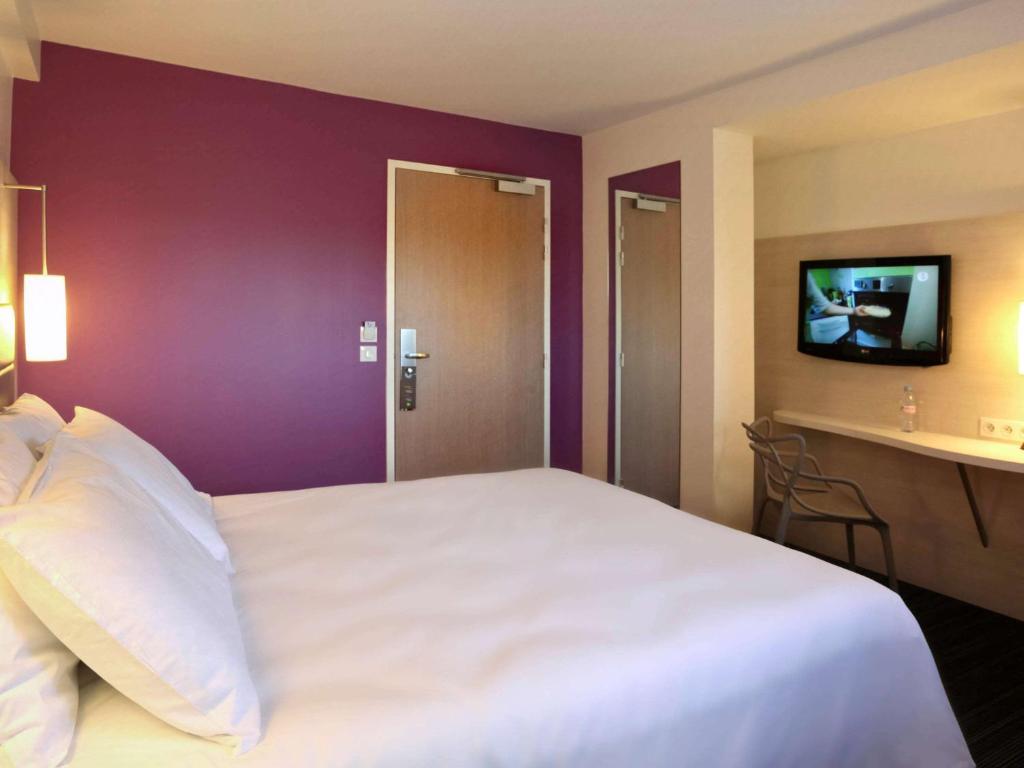 基伯龙基伯龙镇中心宜必思尚品酒店的一间卧室配有一张白色大床和紫色墙壁