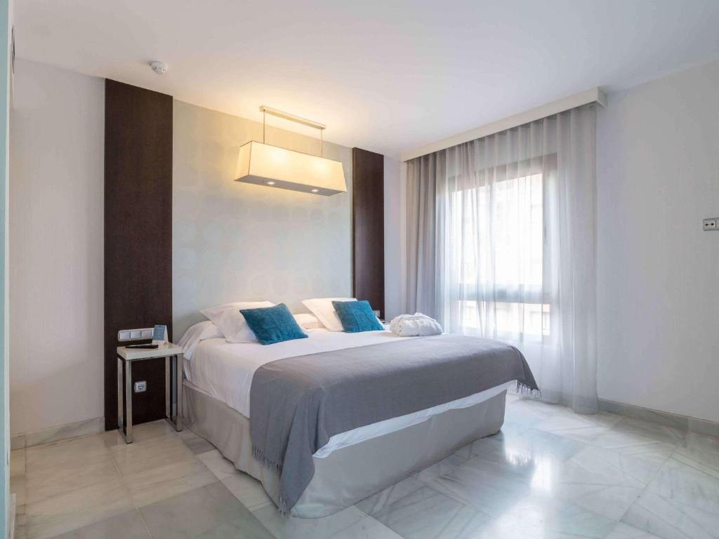 阿尔赫西拉斯Suittes Hotel的一间卧室配有一张带蓝色枕头的床和一扇窗户。