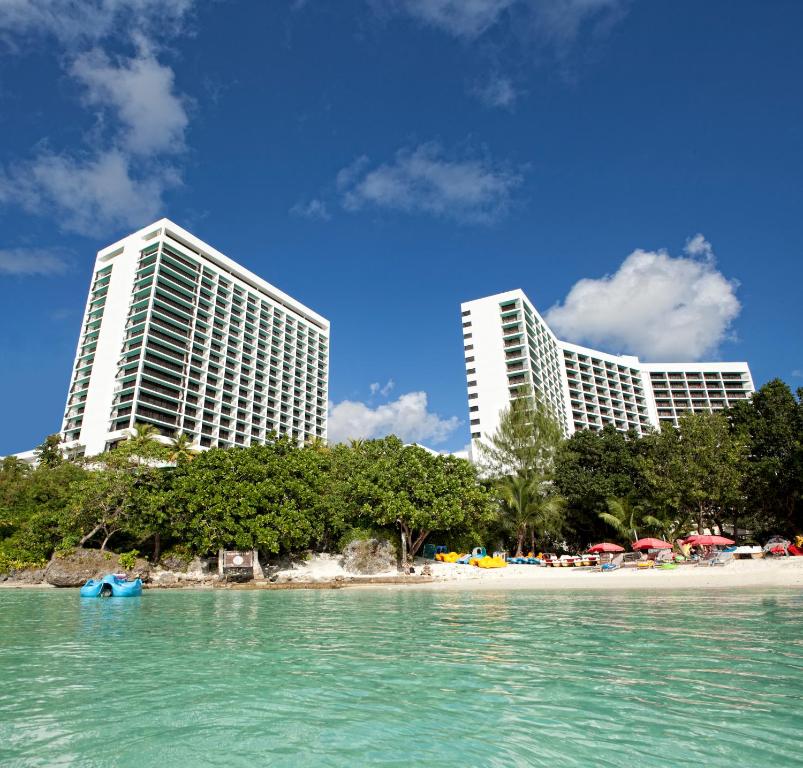 塔穆宁Guam Reef Hotel的海滩上两座高大的建筑,有树木和水