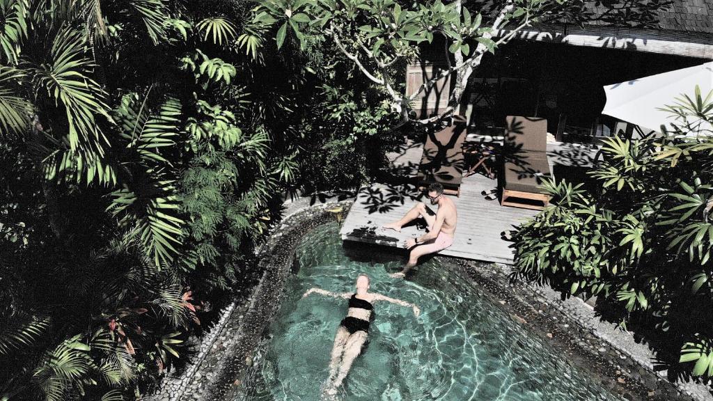 金巴兰JEstate villas & guest houses - Jimbaran的两人在游泳池里,水里养着狗