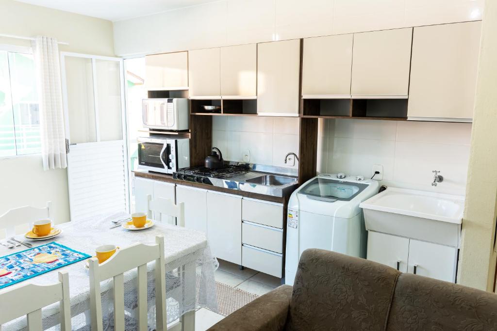 伊塔佩马Apto2 COM AR COND WI-FI E TV SMART的厨房配有白色橱柜、桌子和水槽。