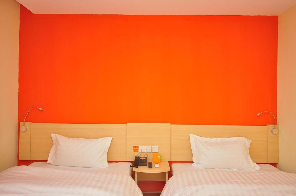 Huadian7天酒店·德州齐河客运中心店的橙色墙壁的客房内的两张床