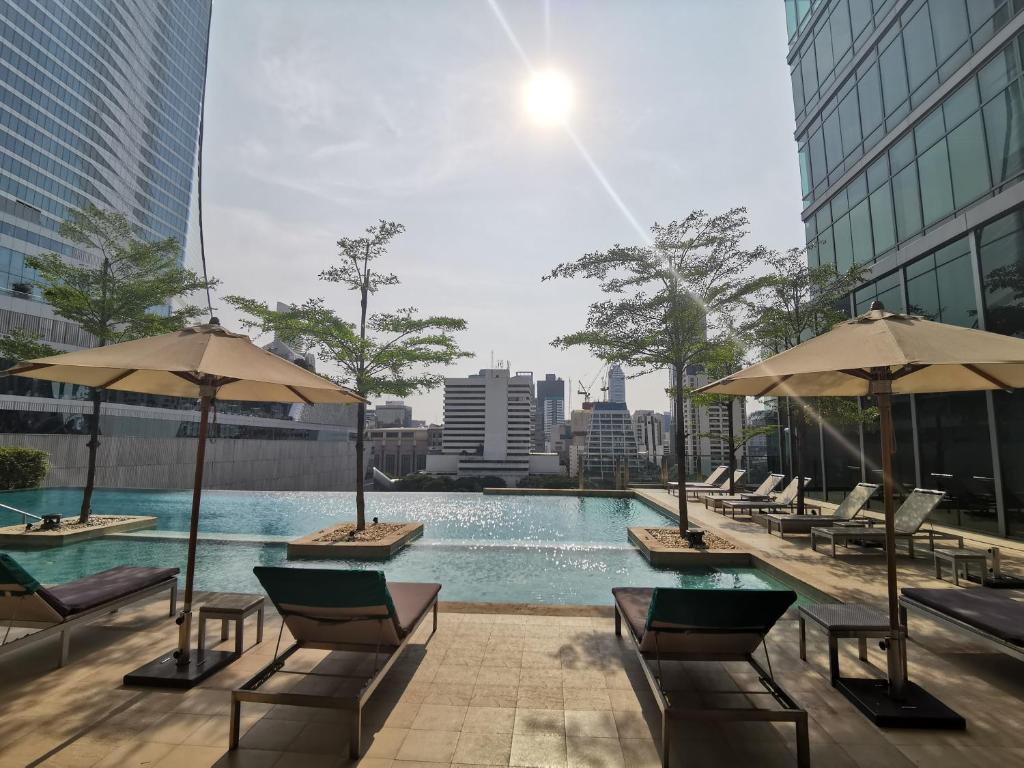 曼谷Sivatel Bangkok Hotel的大楼内一个带椅子和遮阳伞的游泳池