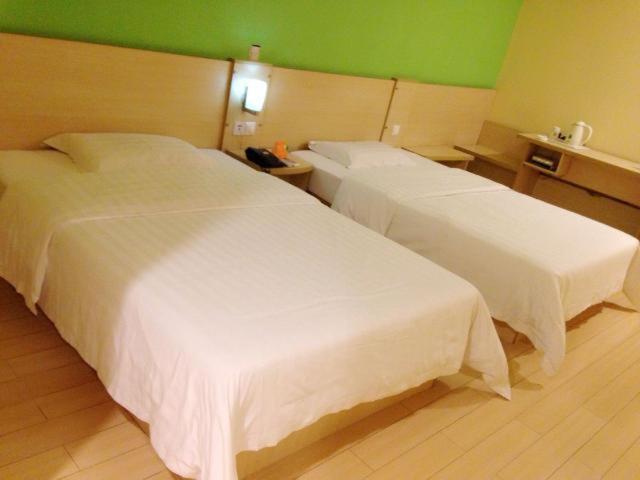 苏州7天酒店·苏州狮山龙湖天街店的酒店客房设有两张床和绿色的墙壁。