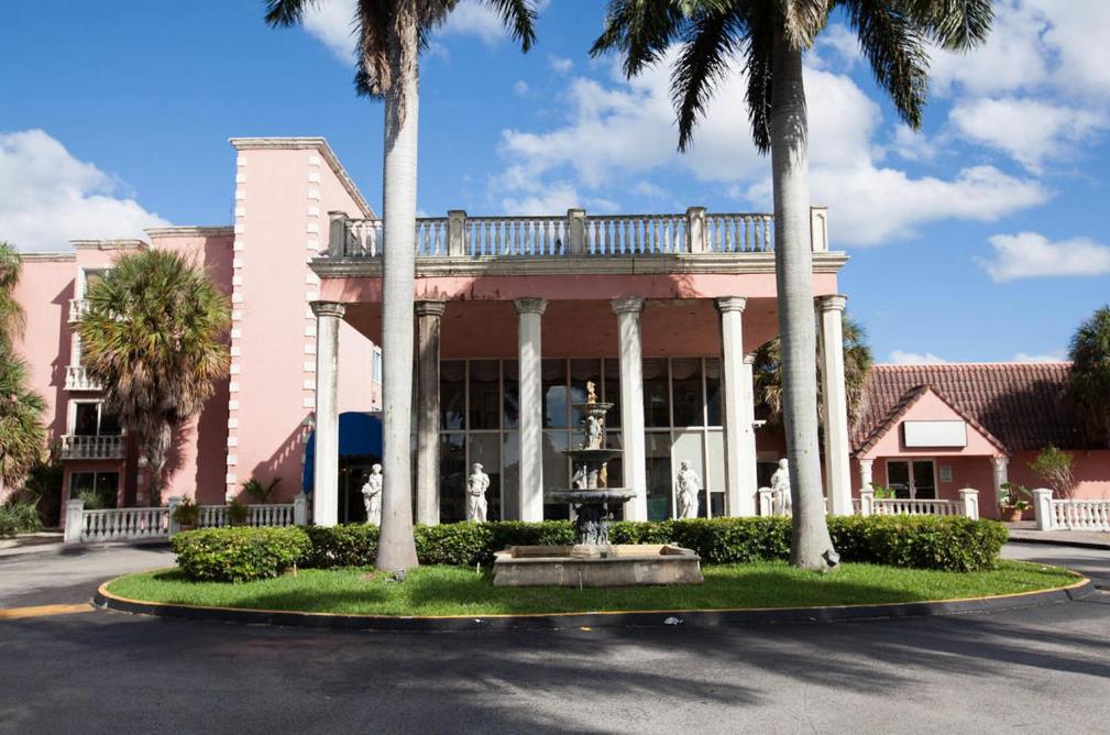 迈阿密Miami Gardens Inn & Suites的一座粉红色的建筑,上面有棕榈树和一个喷泉