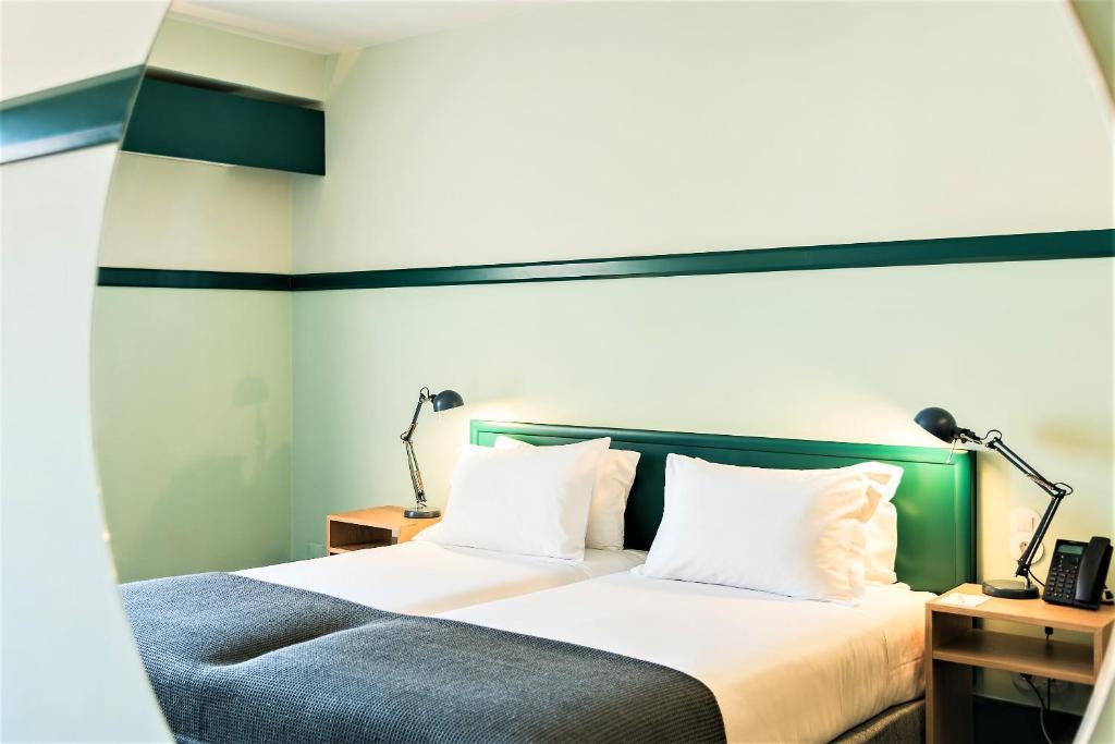 里斯本亚马逊里斯本酒店的一间卧室配有一张带白色床单和两盏灯的床。