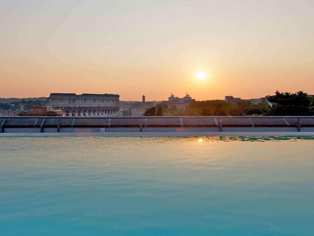 罗马罗马中央斗兽场美居酒店的一大片水,背景是日落
