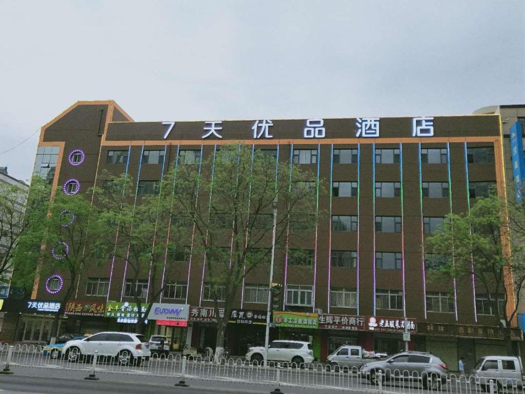 银川7天优品·银川高铁站火车站店的一座大型建筑,前面有汽车停放