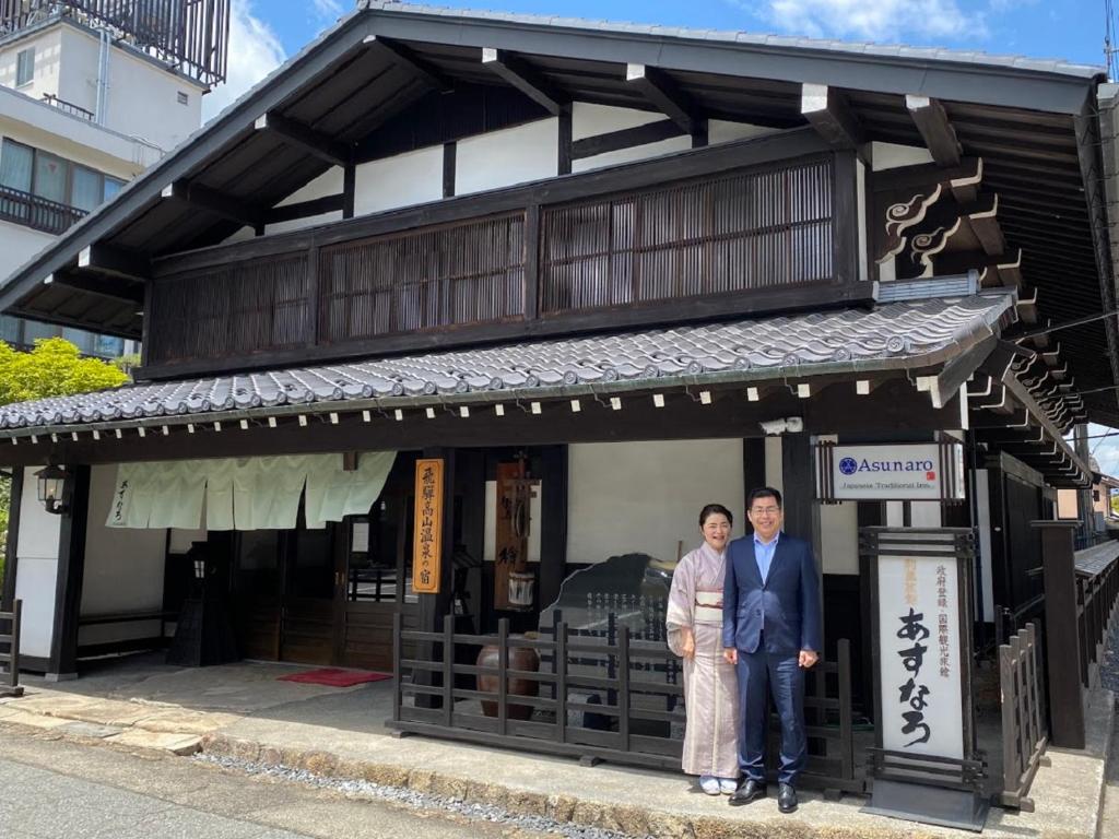高山阿苏娜若日式旅馆的站在建筑物前面的男人和女人