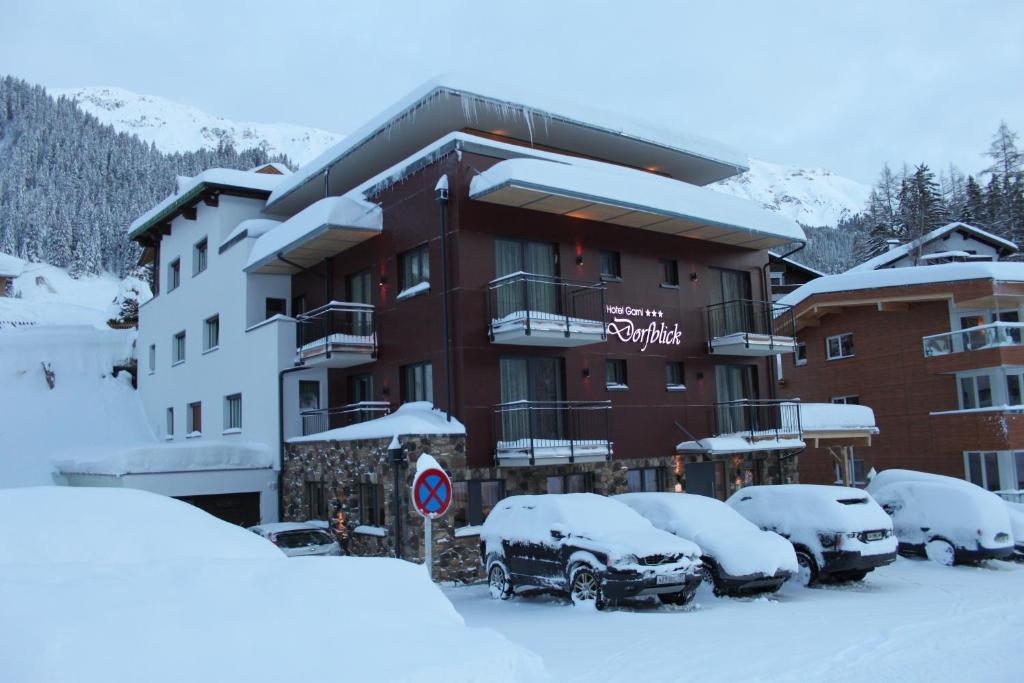 圣安东阿尔贝格Hotel Garni Dorfblick的停车场内有雪盖汽车的建筑