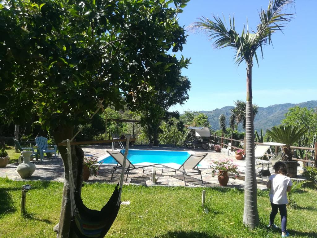 莫塔卡玛斯特拉Le Muse Country House - Gole Alcantara的站在一个院子的游泳池旁,躺着吊床的男孩
