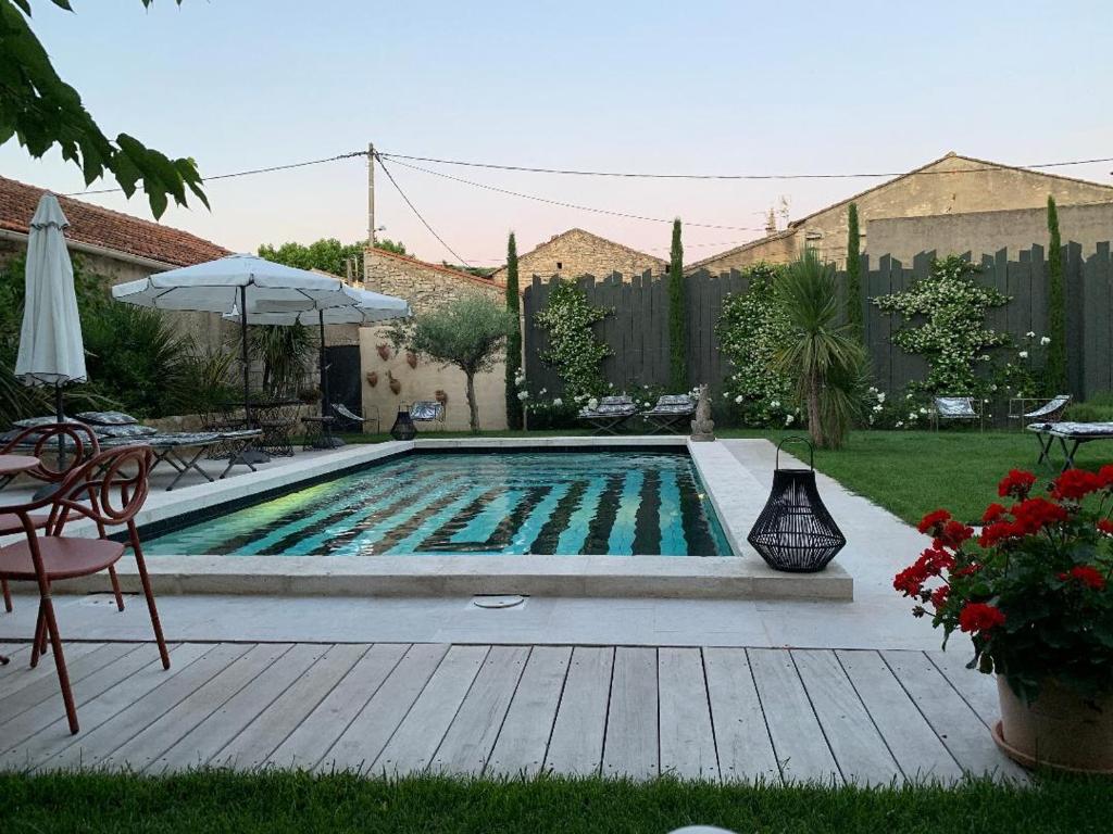 圣雷米普罗旺斯Le petit hotel的庭院内的游泳池,配有桌子和遮阳伞