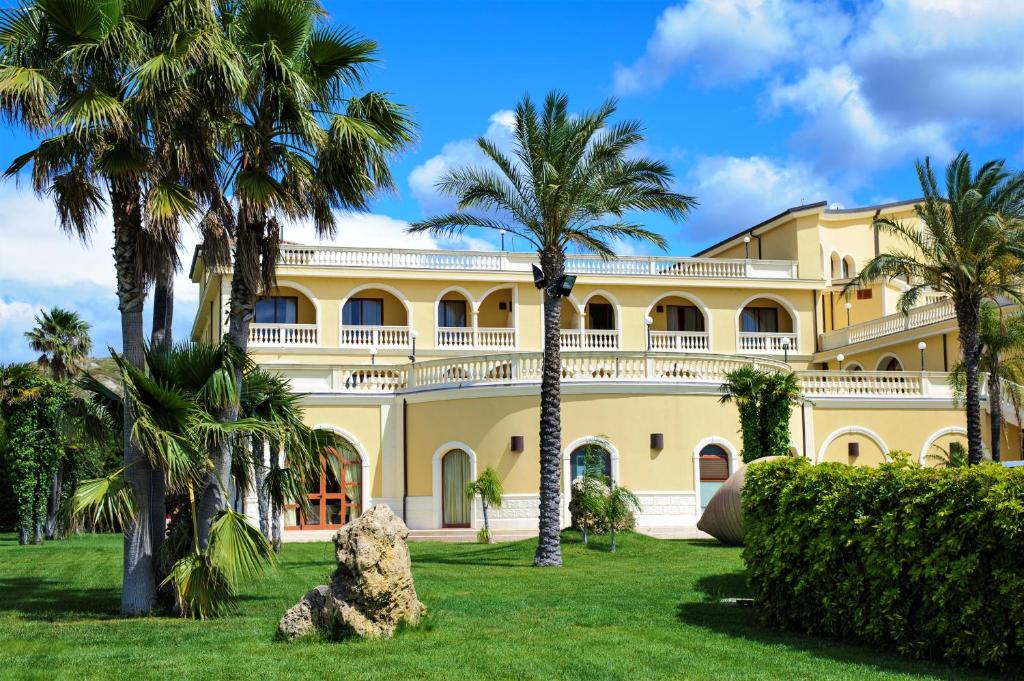 罗切拉伊奥尼卡帕可德普林西皮酒店的一座黄色的大建筑,前面有棕榈树