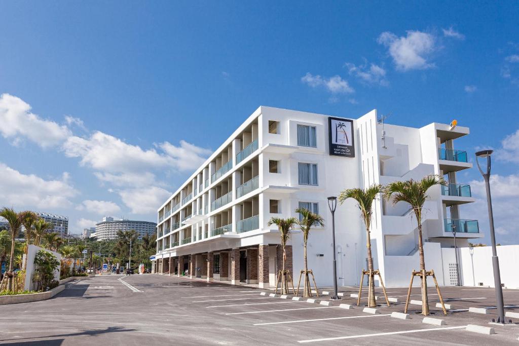 名户Kariyushi LCH. Resort的停车场内一座棕榈树成荫的白色建筑