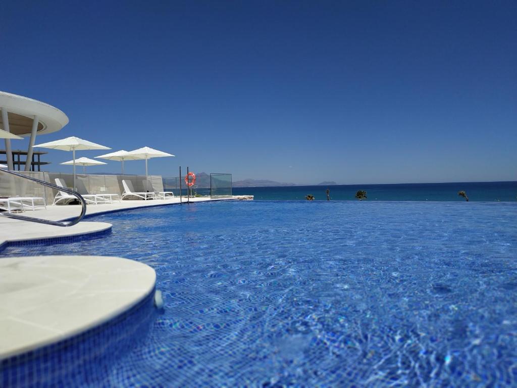 阿利坎特Apartamento SIDI Resort de lujo en Playa San Juan的海滩上带椅子和遮阳伞的游泳池