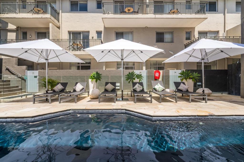拜伦湾拜伦湾公寓式酒店的一个带遮阳伞和椅子的游泳池以及一座建筑
