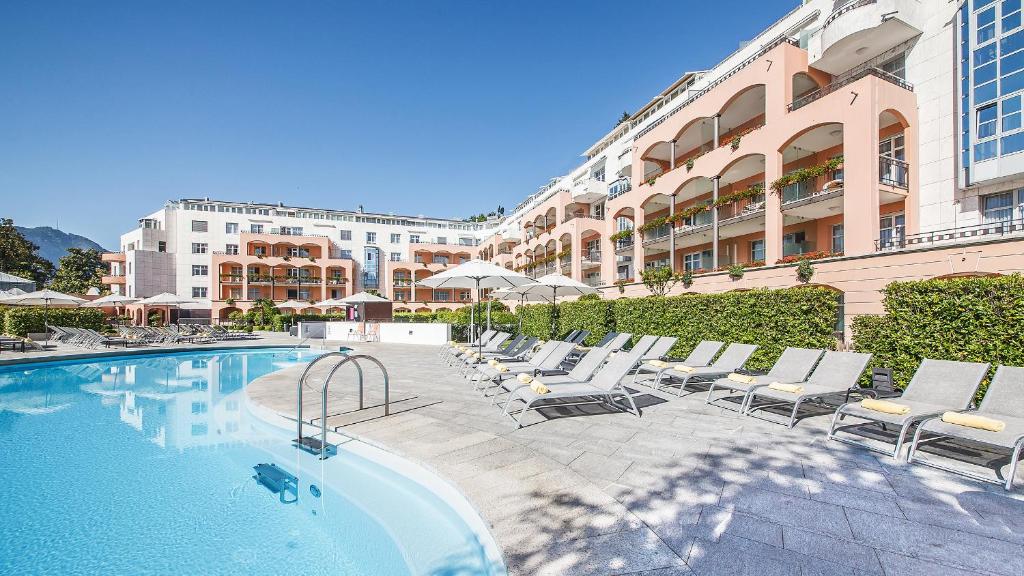 卢加诺Villa Sassa Hotel, Residence & Spa - Ticino Hotels Group的一座带躺椅的游泳池位于大楼旁
