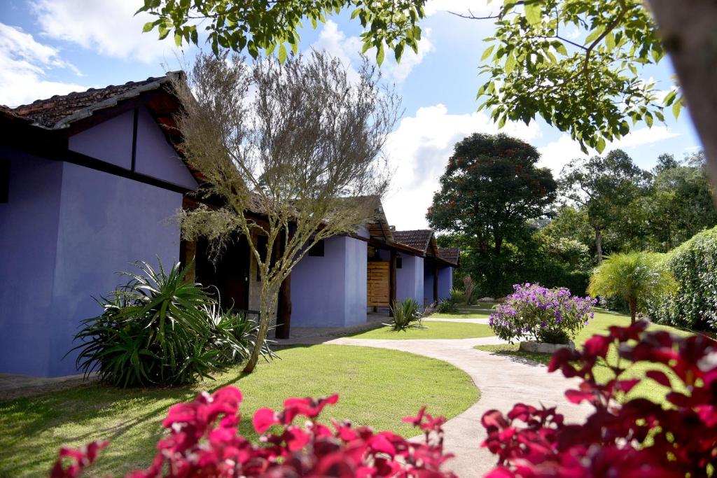 佩德拉阿祖尔Pousada Vale da Mata的一座花园,里面种着房子和一些粉红色的花卉