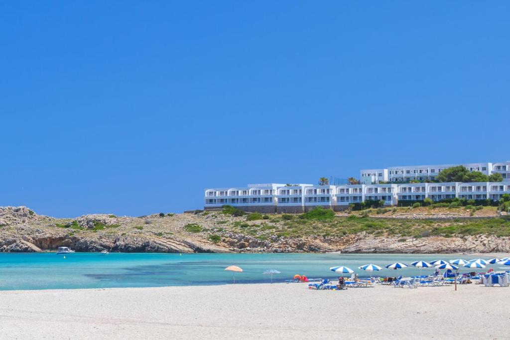 桑帕克Beach Club Menorca的酒店前方的海滩上摆放着椅子和遮阳伞