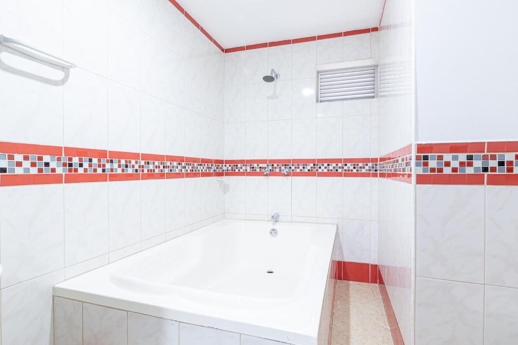 麦德林运动员酒店的浴室设有白色浴缸,铺有红色和白色瓷砖。