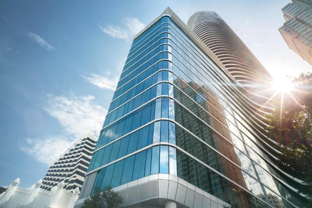 曼谷Magnolias Ratchadamri Boulevard Serviced Residences的天空中阳光灿烂的高高的玻璃建筑