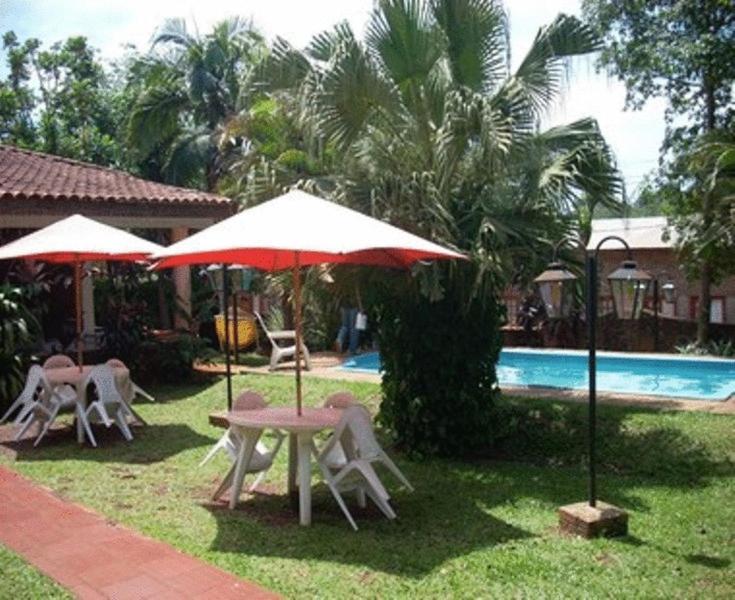 伊瓜苏港El Guembe Hostel House的游泳池畔的桌椅和遮阳伞