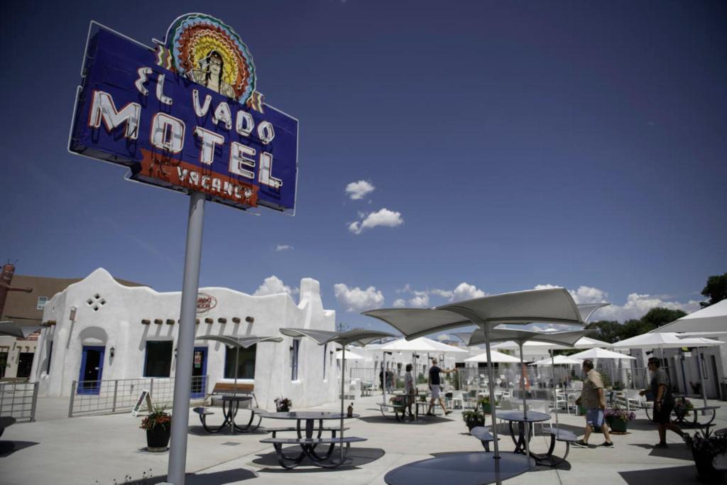 阿尔伯克基El Vado Motel的汽车旅馆前方的标志牌,上面有桌子和遮阳伞