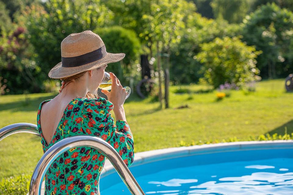 PleškovecHoliday Home Arcadia with pool, hot tub and sauna的戴帽子的女人在游泳池旁的手机上说话